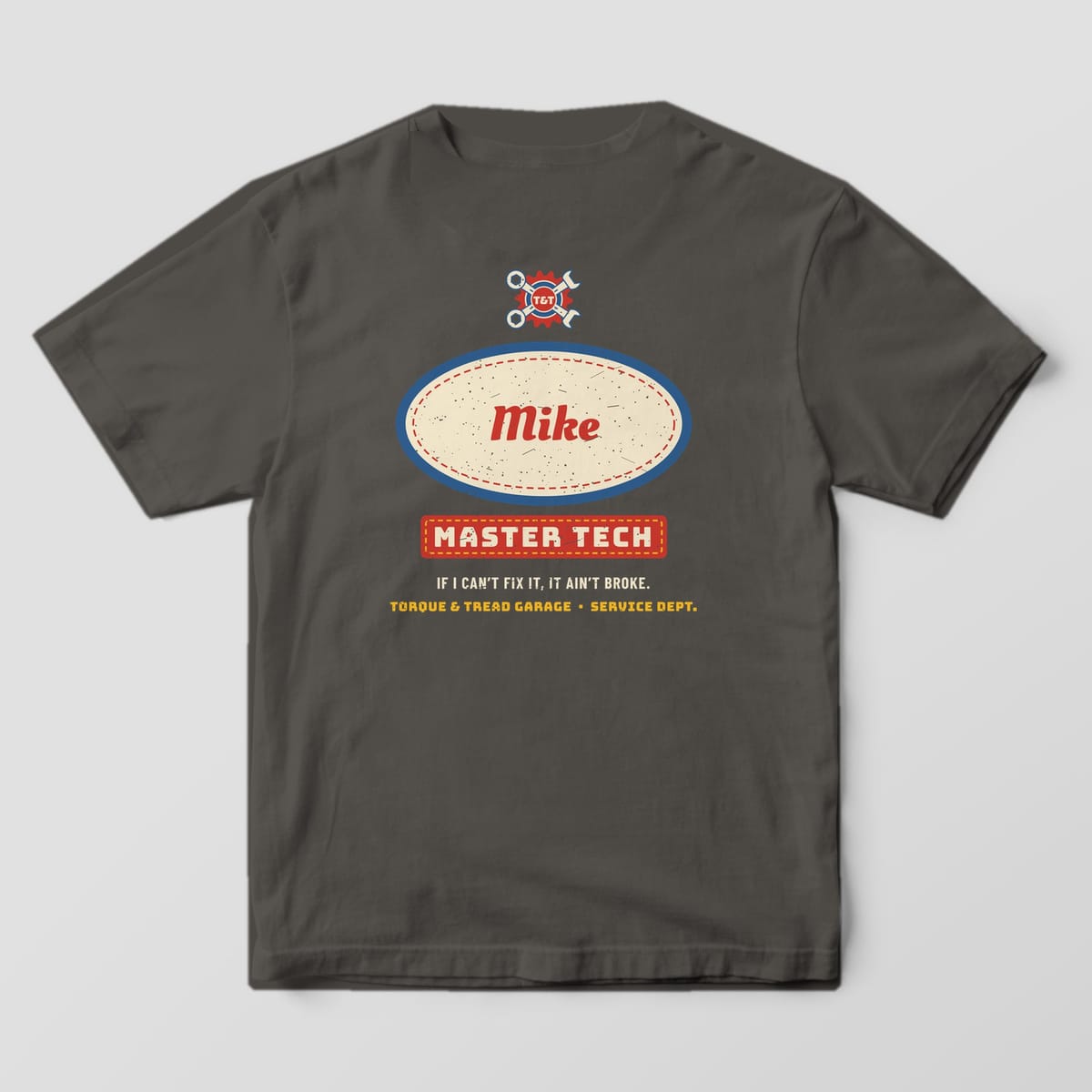 Back of a Pepper Comfort Colors 1717 tee with the cream oval name patch with a blue rim and the name Mike in red script, a red Master Tech stripe and a crossed-wrench crest above.