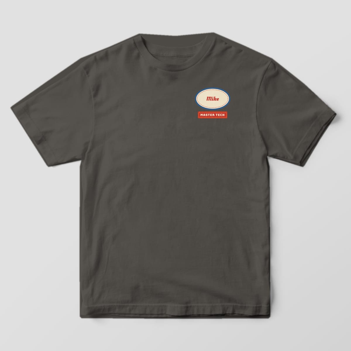 Front of a Pepper Comfort Colors 1717 tee with a small oval name patch with Mike in red script over a Master Tech stripe on the left chest.
