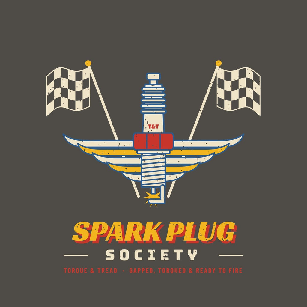 Close-up of the print: spark plug with ribbed insulator, threads and electrode spark, art-deco wings and waving checkered flags, lightly distressed.