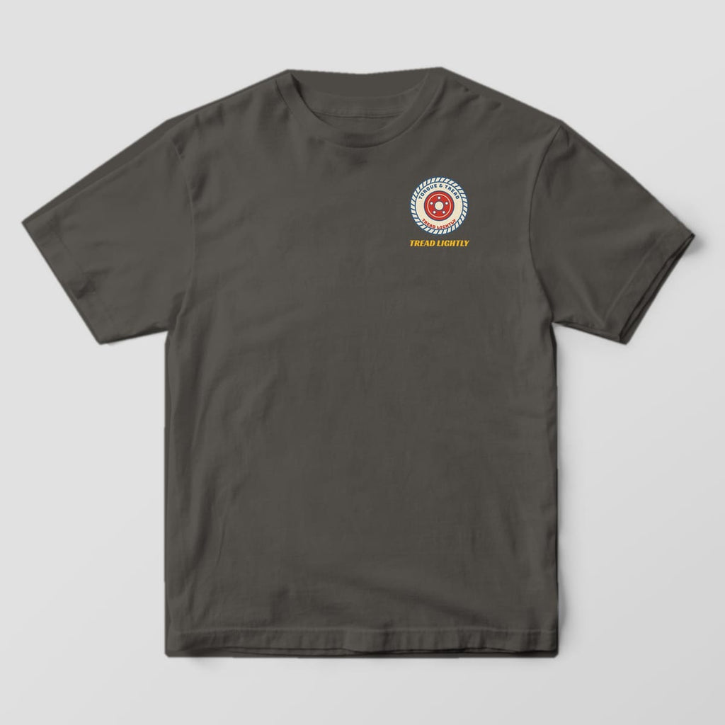 Front of a Pepper Comfort Colors 1717 tee with a small cream tire with blue tread grooves, sidewall lettering and a red five-lug wheel on the left chest.