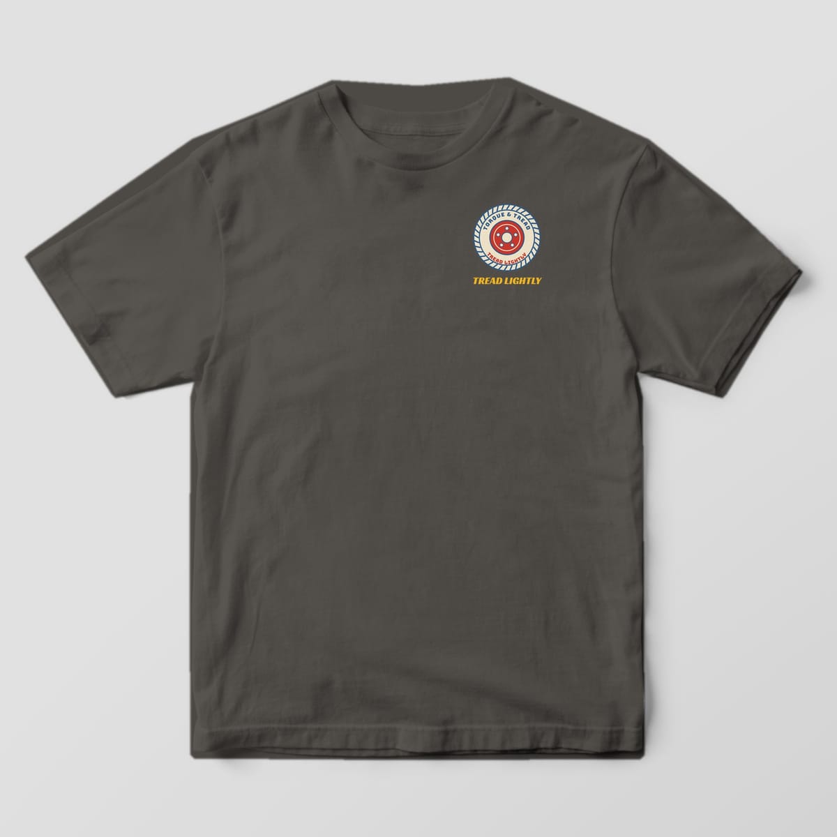 Front of a Pepper Comfort Colors 1717 tee with a small cream tire with blue tread grooves, sidewall lettering and a red five-lug wheel on the left chest.