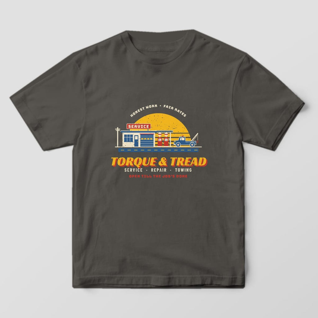 Front of a Pepper Comfort Colors tee with a full-front print of a retro service station at sunset with pumps, a tow truck and Torque & Tread lettering.