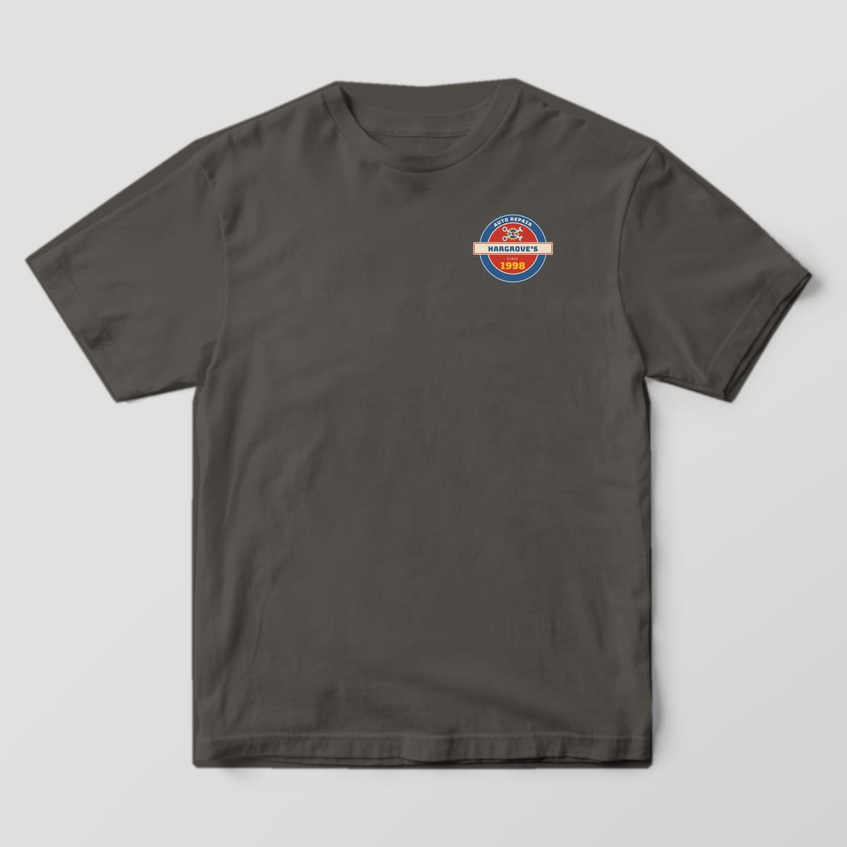 Front of a Pepper Comfort Colors 1717 tee with a small round vintage shop sign with a custom shop name and year on the left chest.