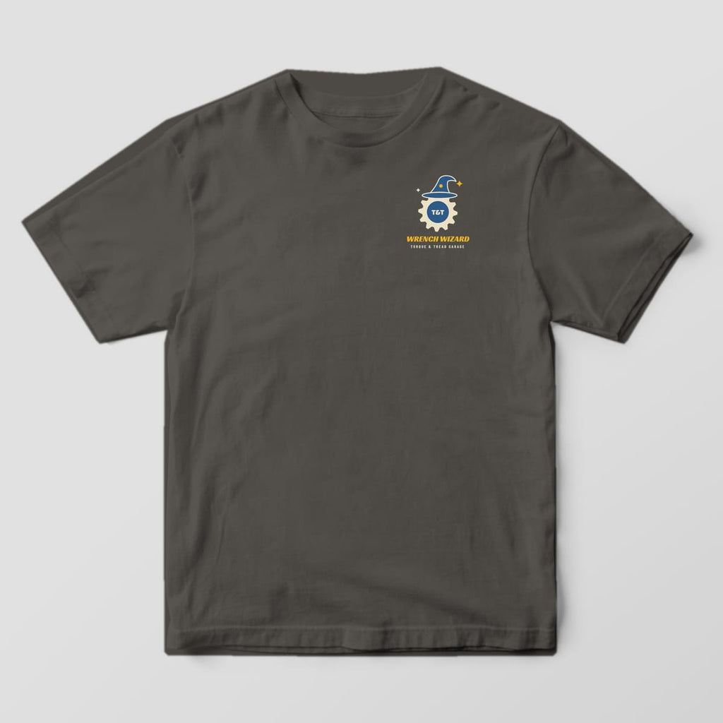 Front of a Pepper Comfort Colors 1717 tee with a small gear wearing a blue wizard hat and the words Wrench Wizard on the left chest.