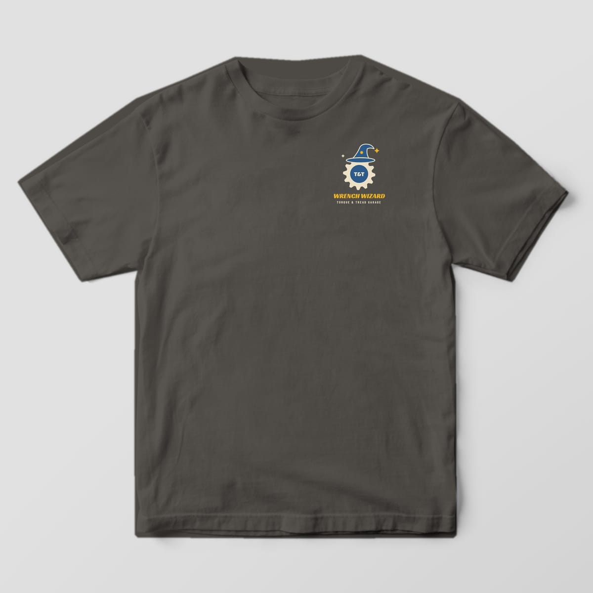 Front of a Pepper Comfort Colors 1717 tee with a small gear wearing a blue wizard hat and the words Wrench Wizard on the left chest.