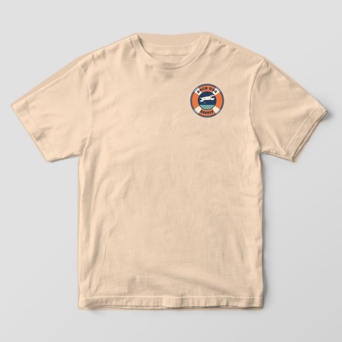 Front of an ivory Comfort Colors tee with a small orange and cream life-ring badge with a leaping dog