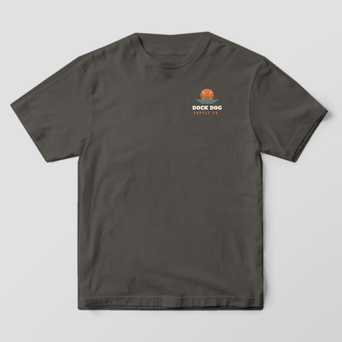 Front of a pepper Comfort Colors tee with a small tennis-ball sun over waves and Dock Dog Supply Co. on the left chest
