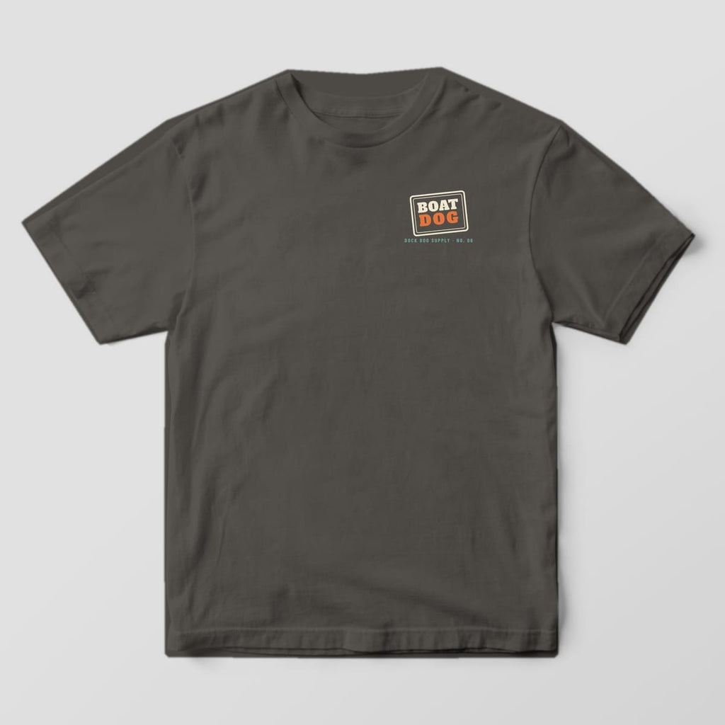 Front of a pepper Comfort Colors tee with a small cream and orange Boat Dog stamp on the left chest