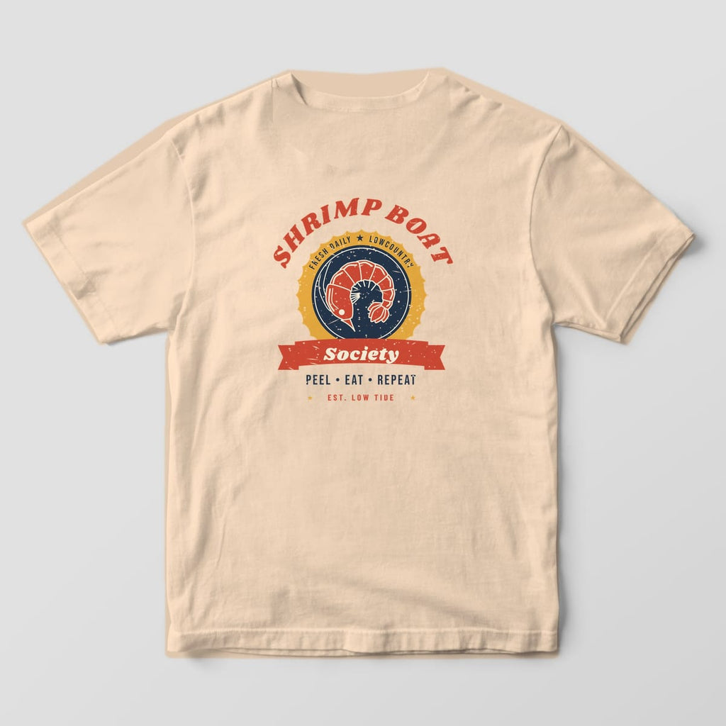 Back of an Ivory Comfort Colors 1717 tee with a red, gold and navy shrimp badge, SHRIMP BOAT arched above, a red Society banner and PEEL EAT REPEAT below.