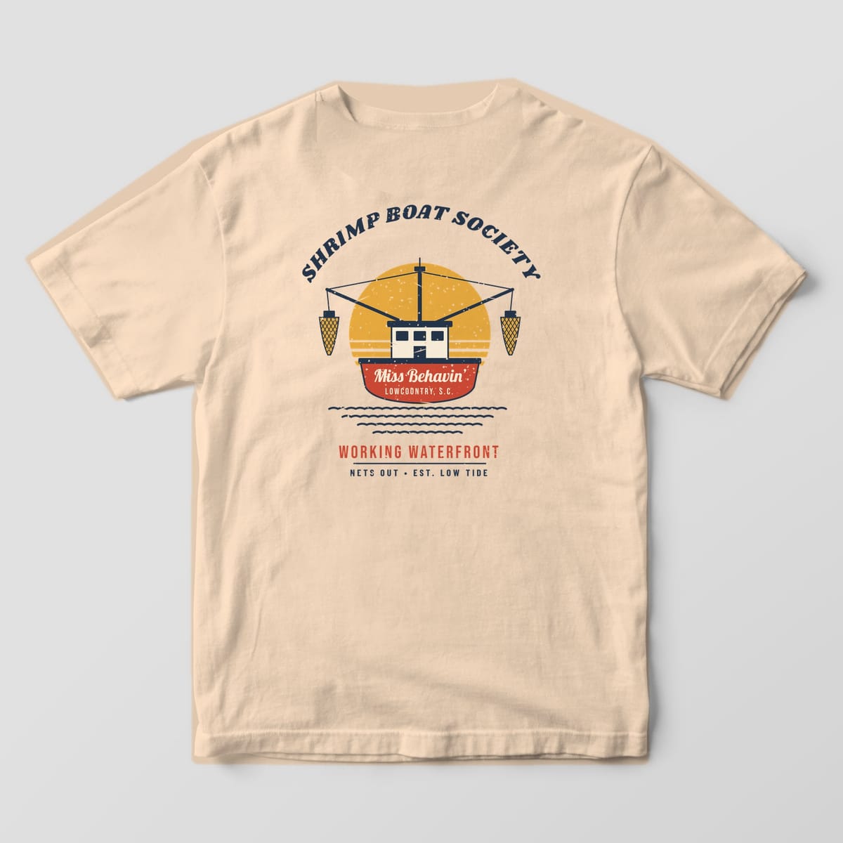 Back of an Ivory Comfort Colors 1717 tee with a red shrimp boat named Miss Behavin', outriggers and gold nets against a striped sunrise.