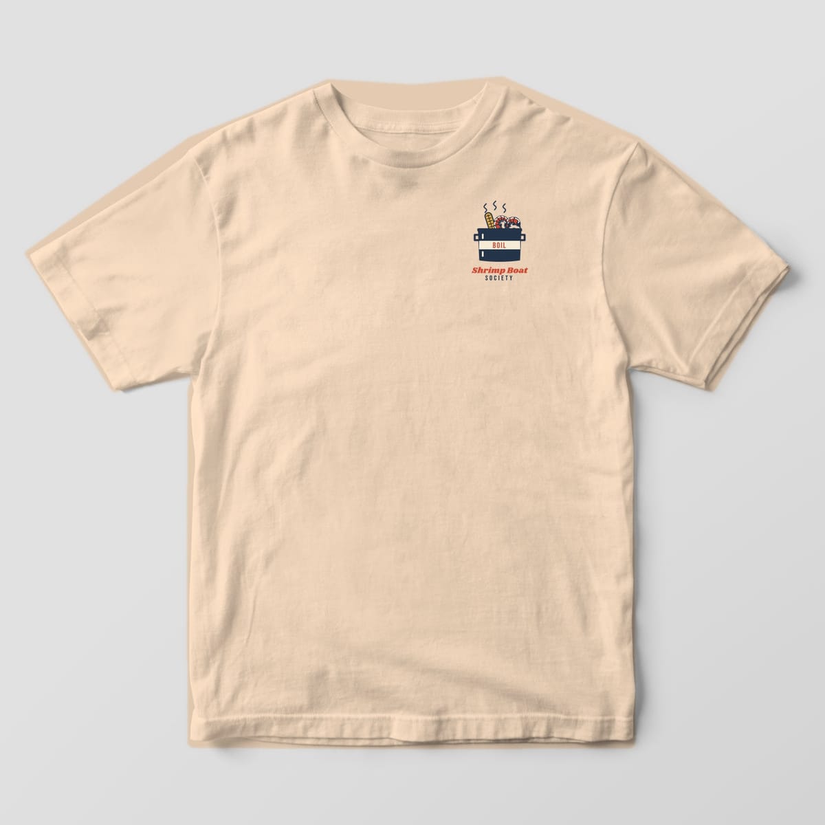 Front of an Ivory Comfort Colors 1717 tee with a small navy boil pot holding corn and shrimp above the words Shrimp Boat Society.