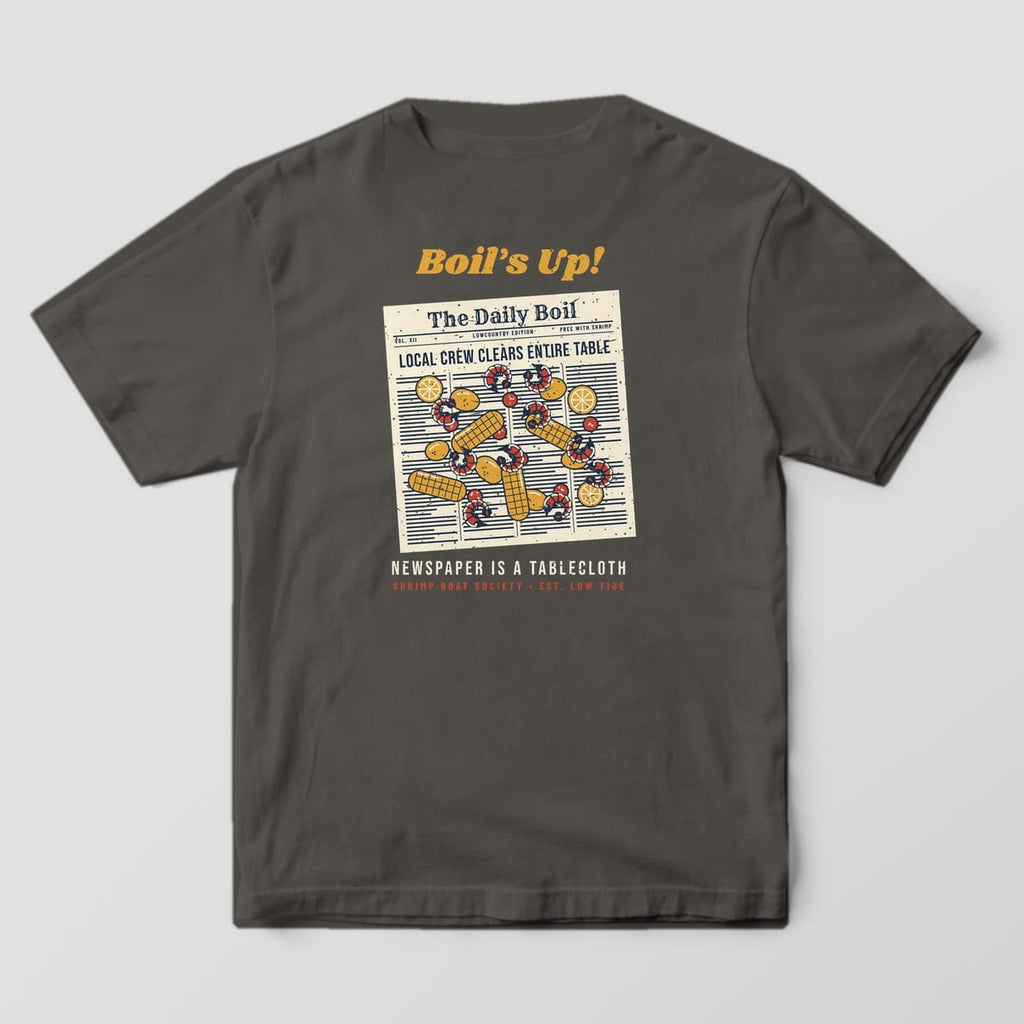 Back of a Pepper Comfort Colors 1717 tee with a cream newspaper covered in red shrimp, gold corn, potatoes, sausage and lemons under the words Boil's Up!