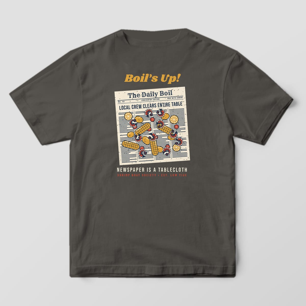 Back of a Pepper Comfort Colors 1717 tee with a cream newspaper covered in red shrimp, gold corn, potatoes, sausage and lemons under the words Boil's Up!