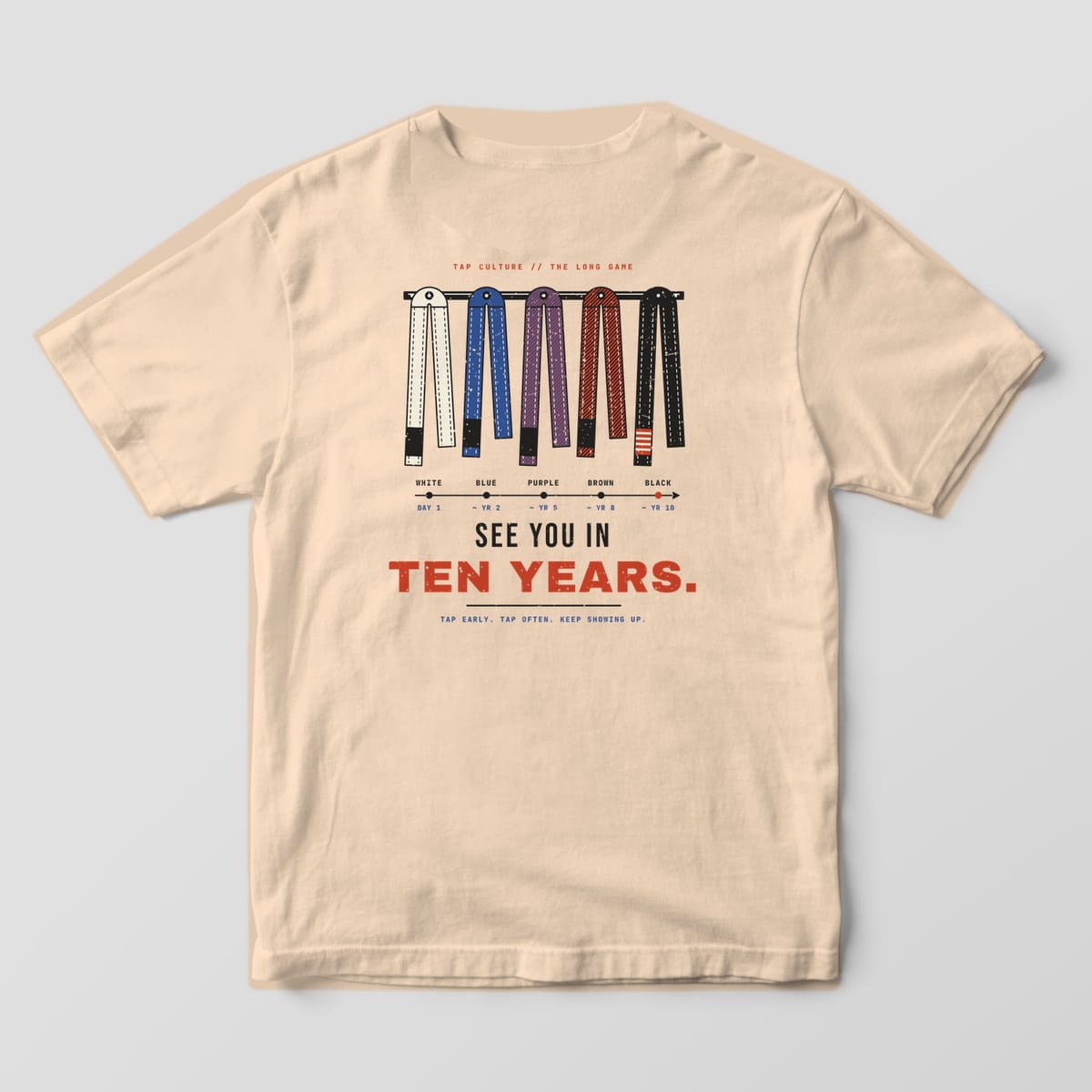 Back of an ivory Comfort Colors 1717 tee with white, blue, purple, brown and black belts on a peg rail and a rank timeline.