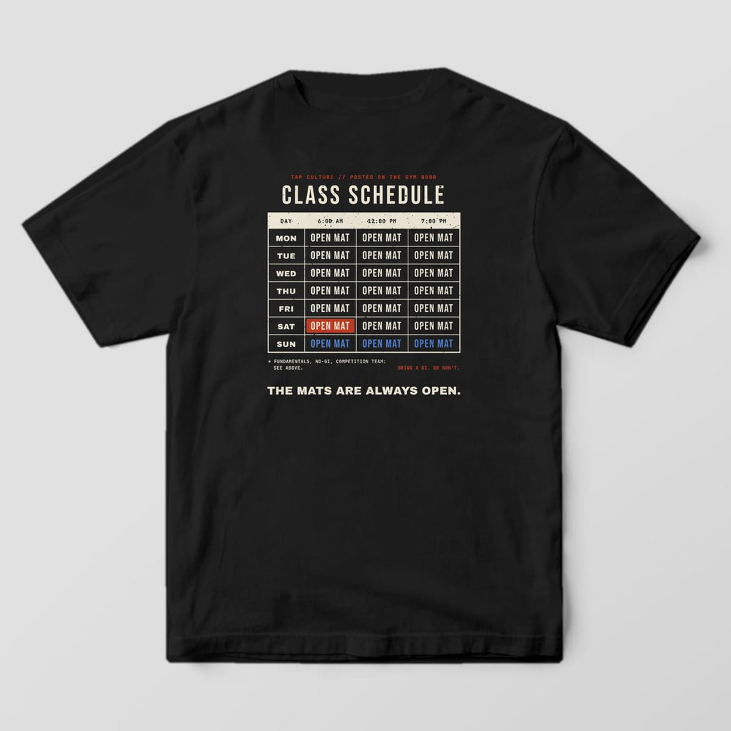 Back of a black Comfort Colors 1717 tee with a cream schedule grid, every day and time reading OPEN MAT.