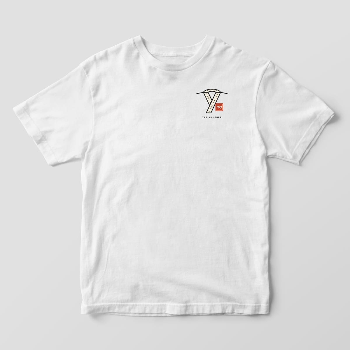 Front of a white Comfort Colors 1717 tee with a crossed gi collar drawing, a red TC seal and TAP CULTURE on the left chest.