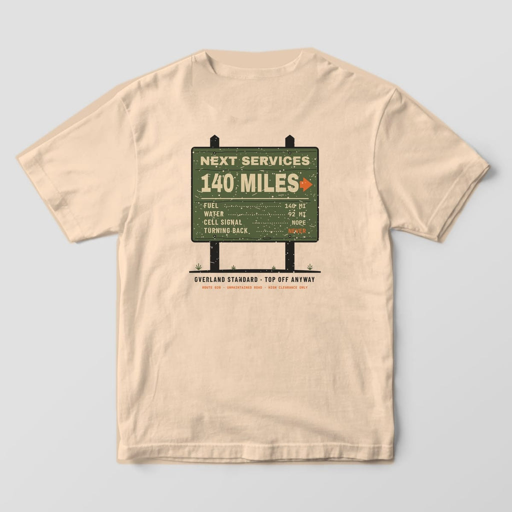 Back of a Ivory Comfort Colors 1717 tee with an olive trailhead sign on posts reading Next Services 140 Miles, Fuel, Water, Cell Signal Nope, Turning Back Never.