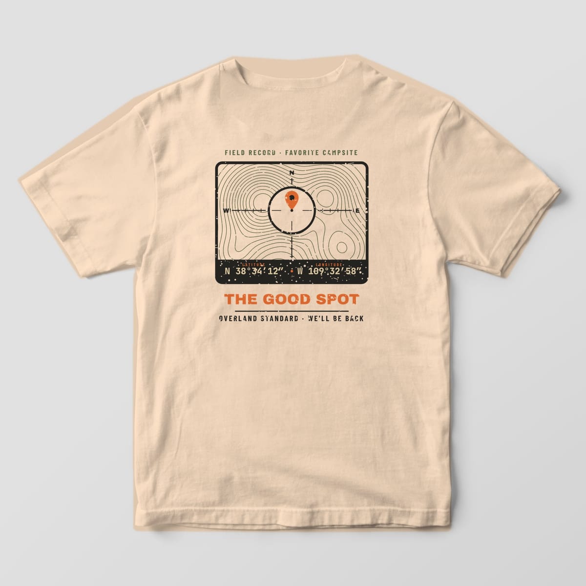 Back of a ivory Comfort Colors 1717 T-shirt showing a topo map coordinate badge with a crosshair, orange map pin, latitude and longitude and the words The Good Spot