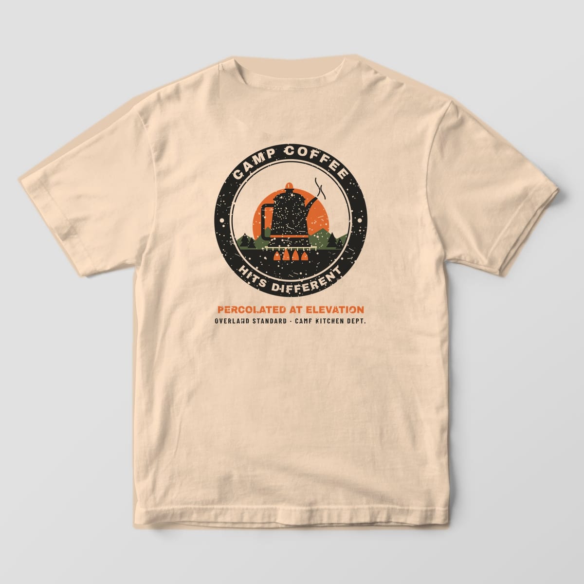 Back of a ivory Comfort Colors 1717 T-shirt showing a round badge with a speckled enamel percolator over a campfire at sunrise and the words Camp Coffee Hits Different