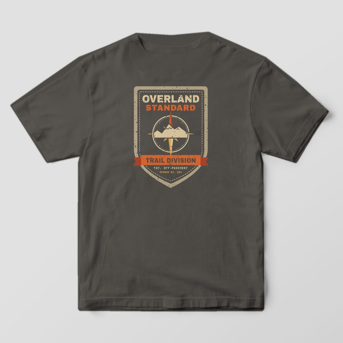Back of a pepper Comfort Colors 1717 T-shirt showing a vintage stitched shield patch with a compass rose and mountains, a Trail Division ribbon and the words Overland Standard