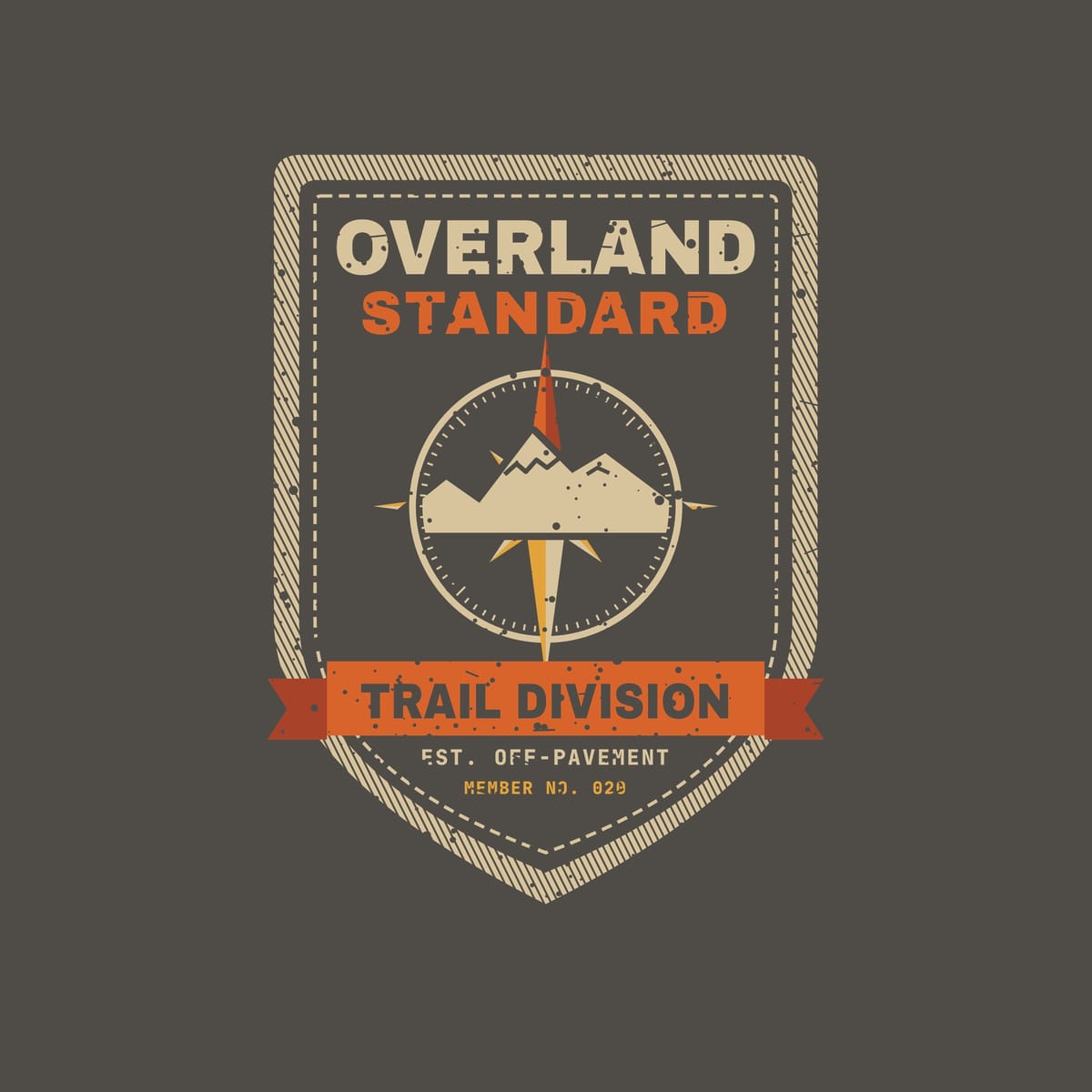 Close-up of the back print artwork on a pepper background: a vintage stitched shield patch with a compass rose and mountains, a Trail Division ribbon and the words Overland Standard