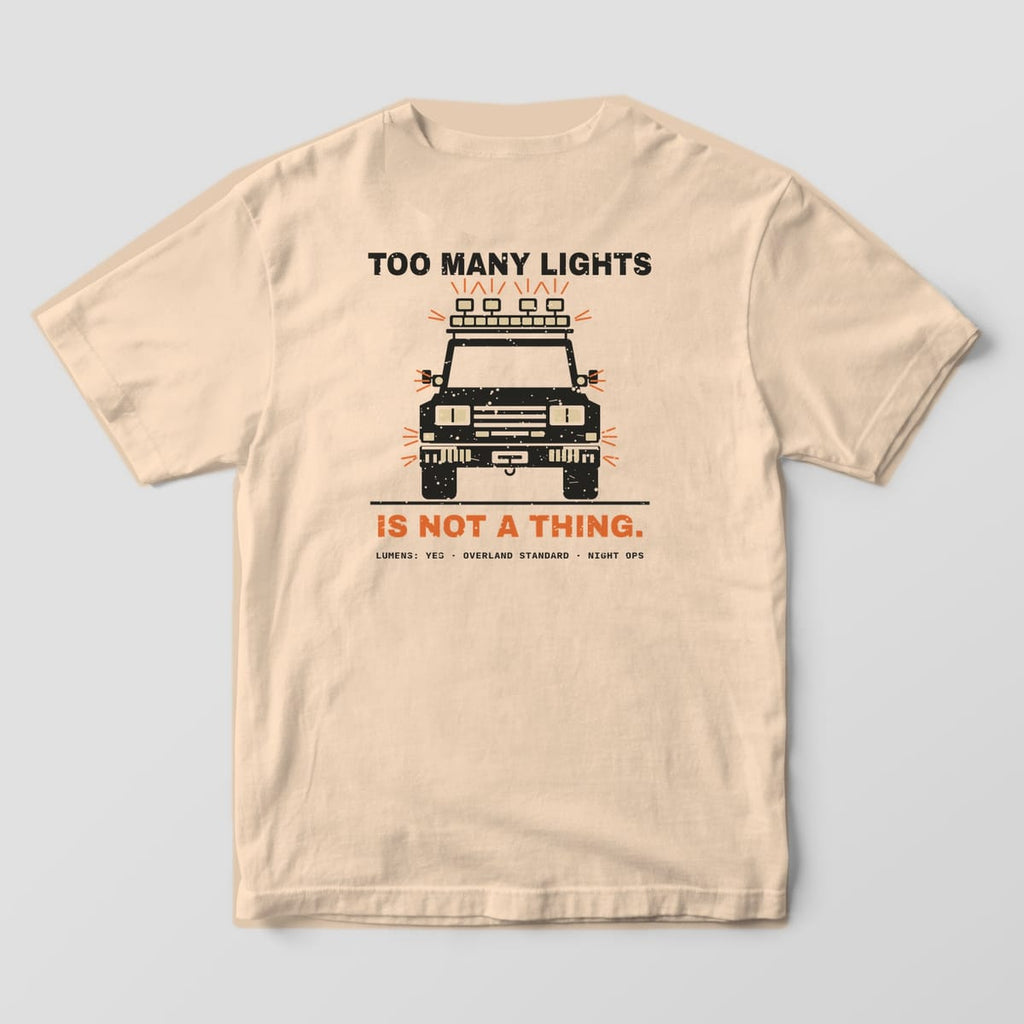 Back of a ivory Comfort Colors 1717 T-shirt showing a front view of a boxy truck covered in auxiliary lights with rays and the words Too Many Lights Is Not a Thing