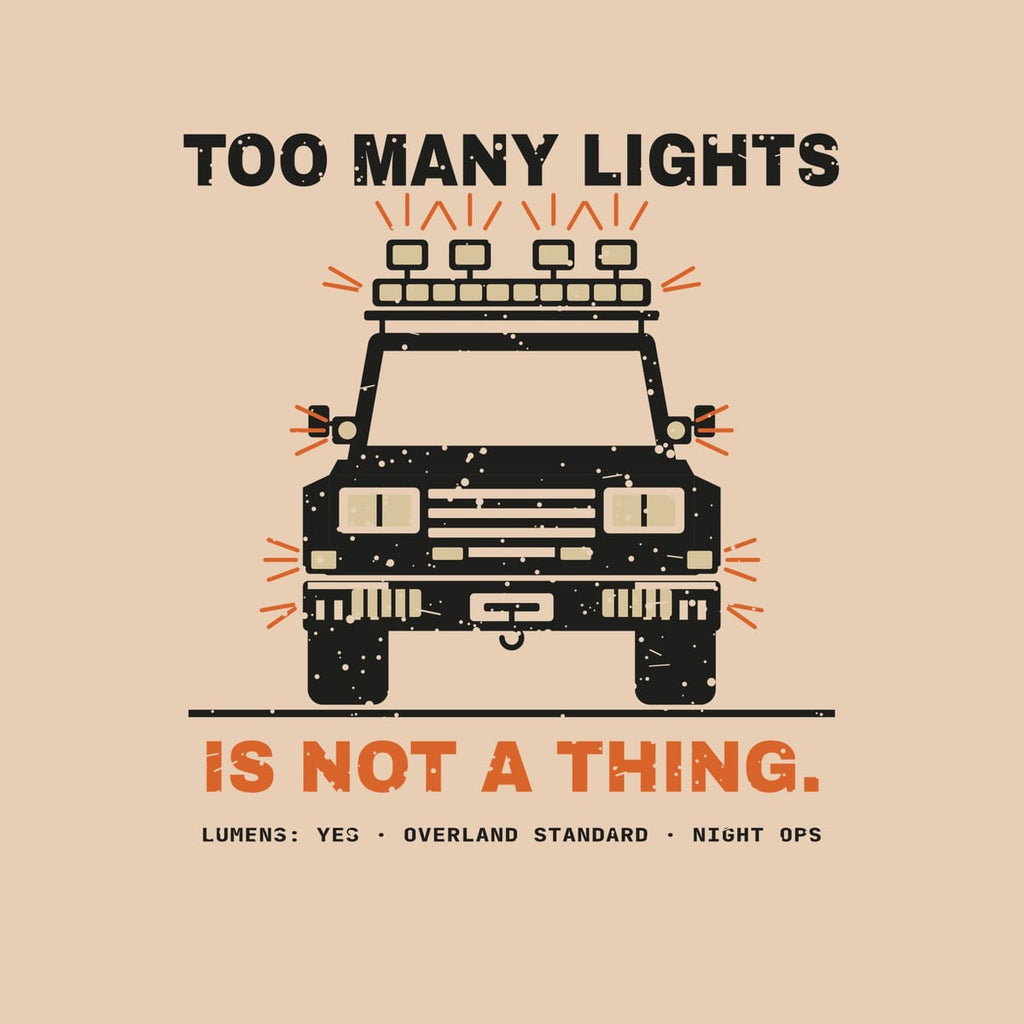 Close-up of the back print artwork on a ivory background: a front view of a boxy truck covered in auxiliary lights with rays and the words Too Many Lights Is Not a Thing