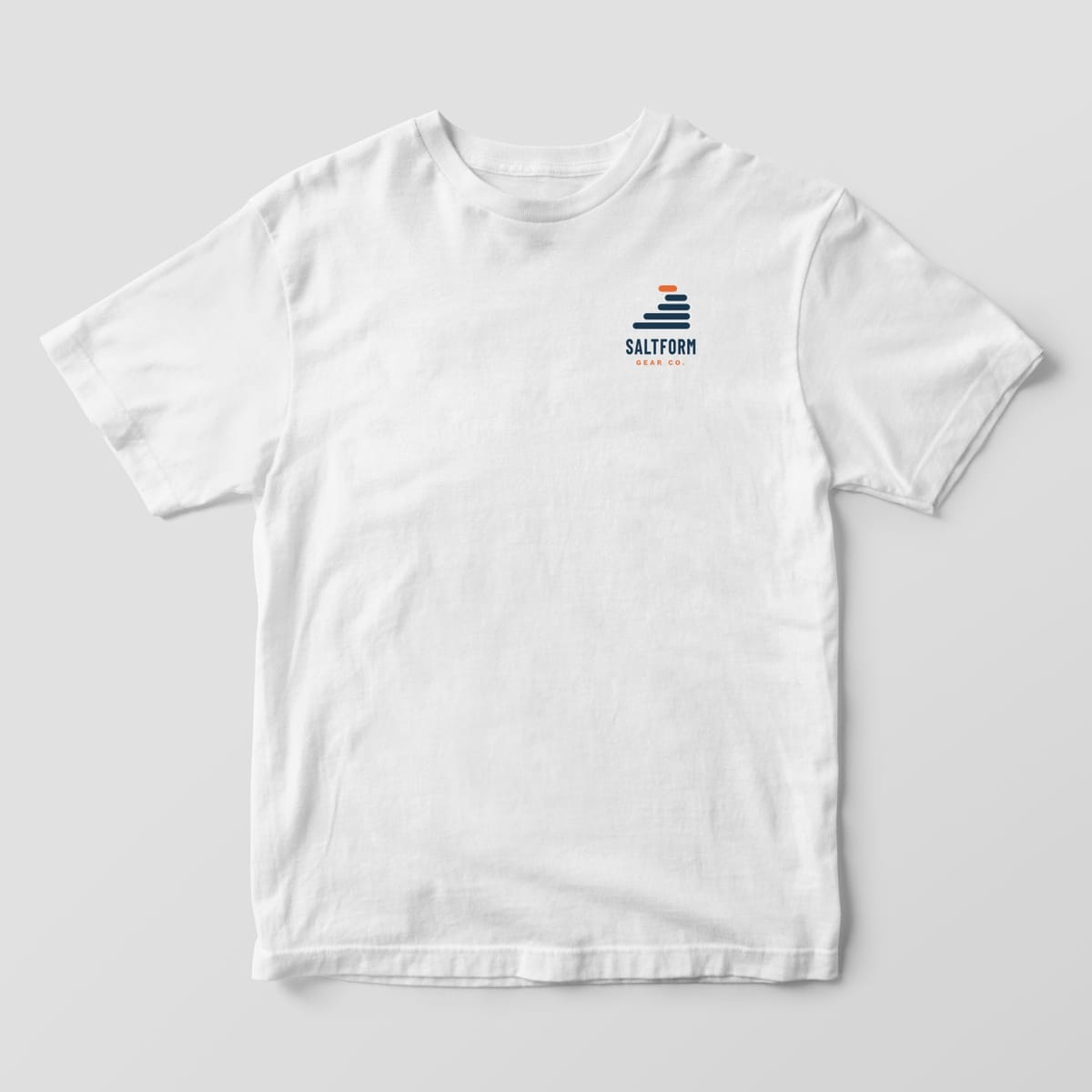 Front of a white Comfort Colors 1717 tee with a small navy and orange layer-wave logo and SALTFORM GEAR CO. on the left chest.