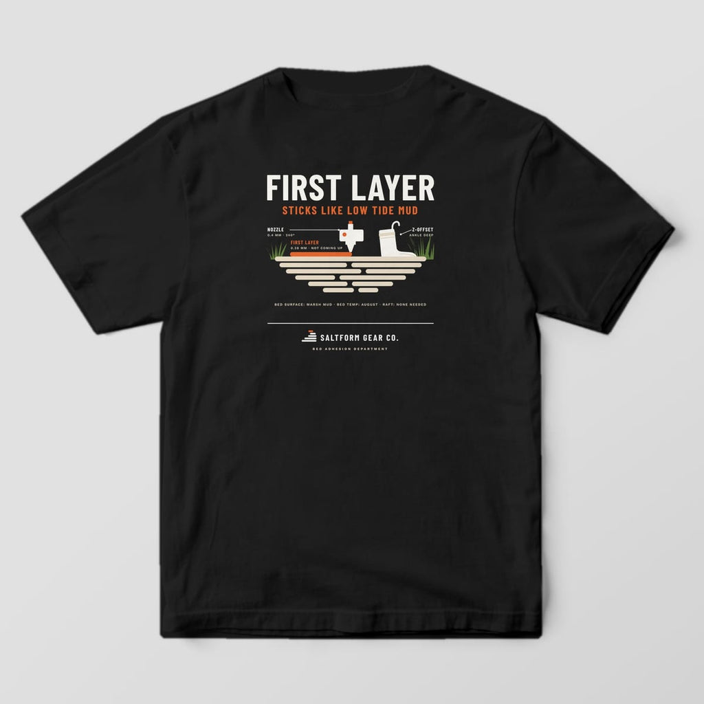 Back of a black Comfort Colors 1717 tee with a 3D printer nozzle laying a first layer onto marsh mud beside a stuck boot.