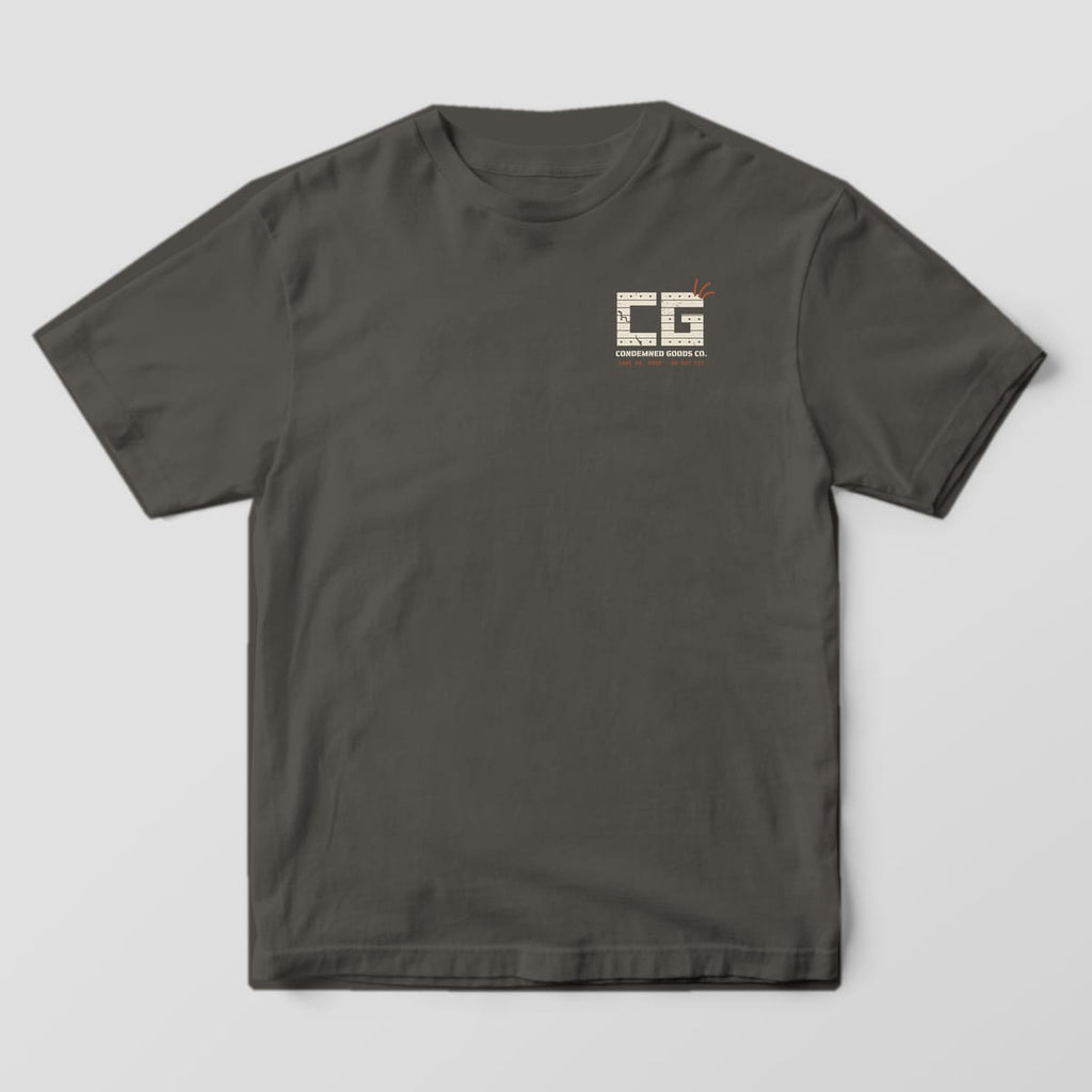 Front of a pepper Comfort Colors 1717 tee with a small cream concrete-block CG monogram and rust rebar on the left chest.