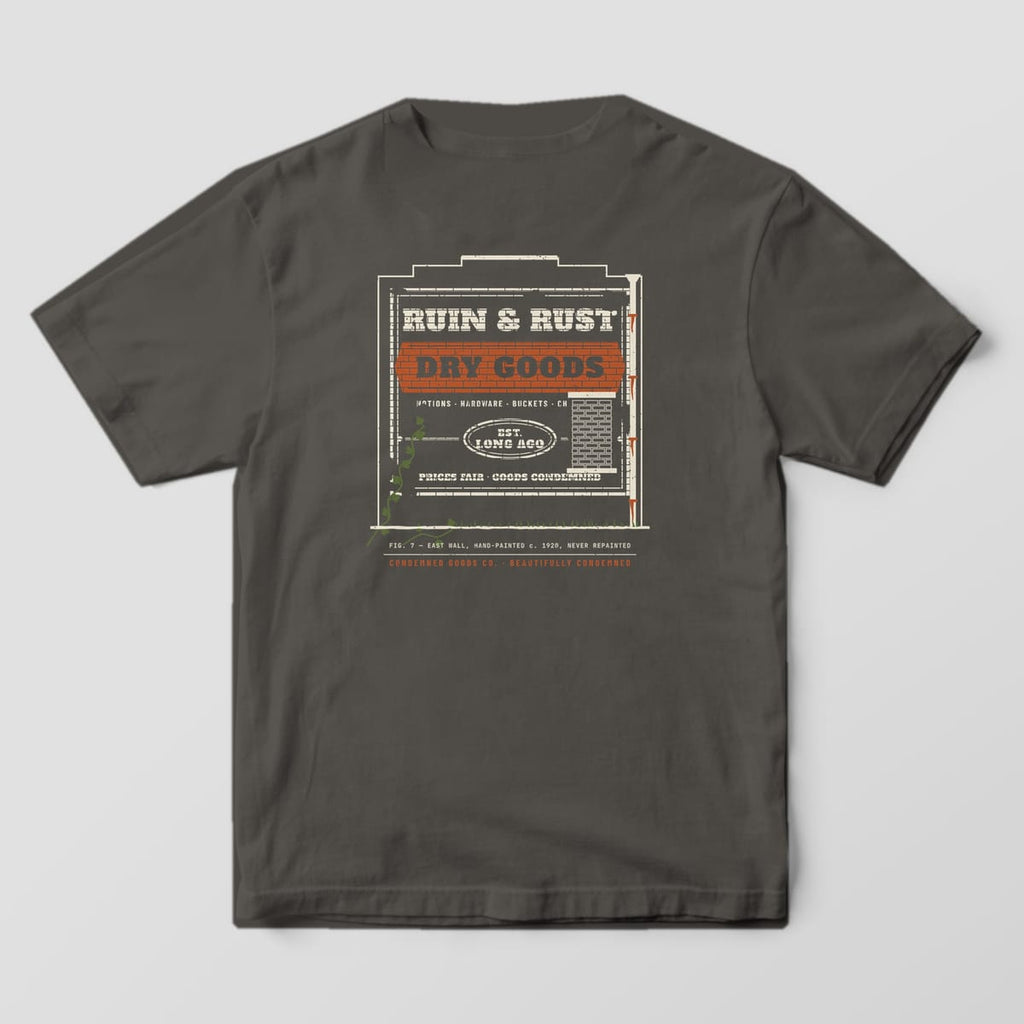 Back of a pepper Comfort Colors 1717 tee with a faded brick-wall ghost sign print reading Ruin & Rust Dry Goods, Est. Long Ago.