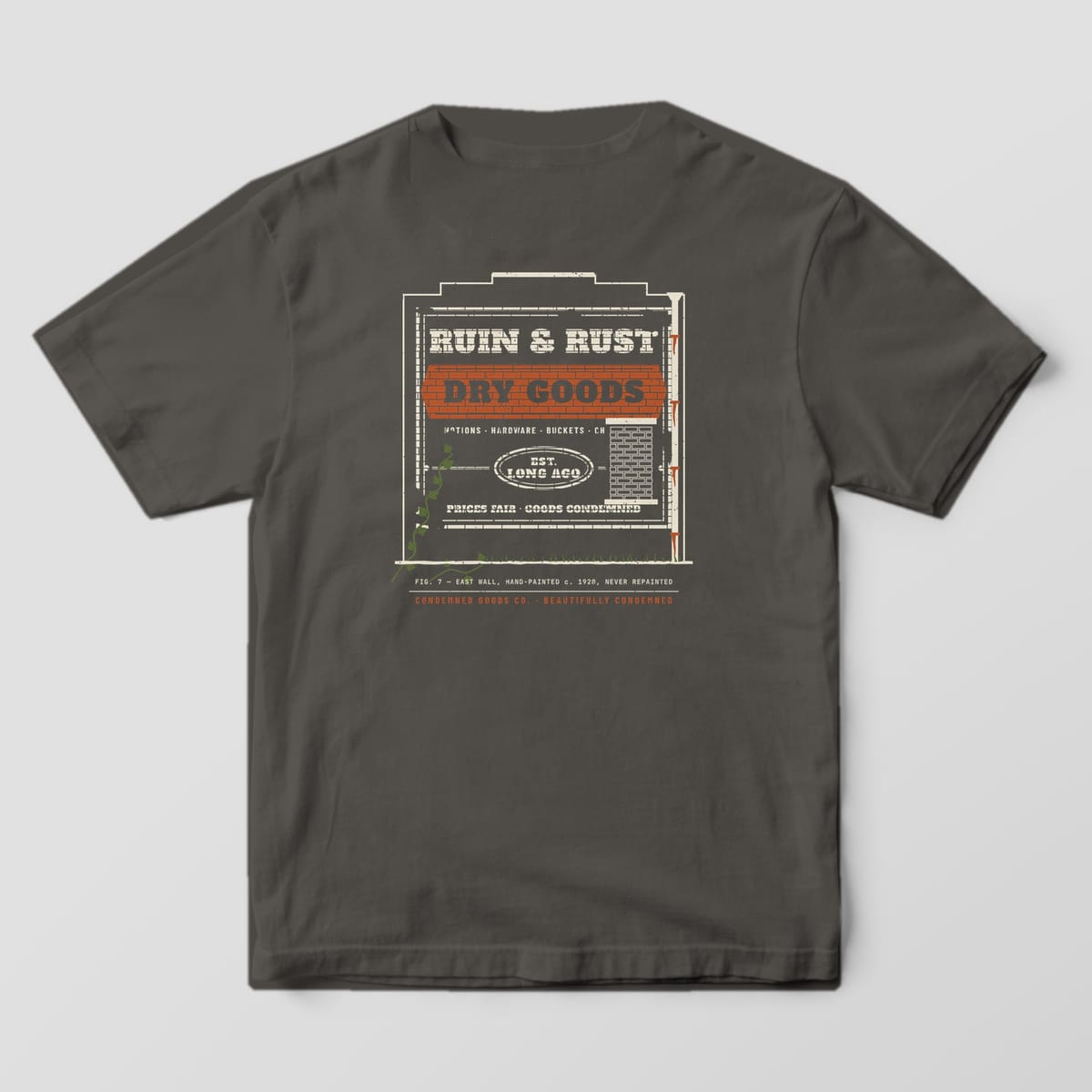 Back of a pepper Comfort Colors 1717 tee with a faded brick-wall ghost sign print reading Ruin & Rust Dry Goods, Est. Long Ago.