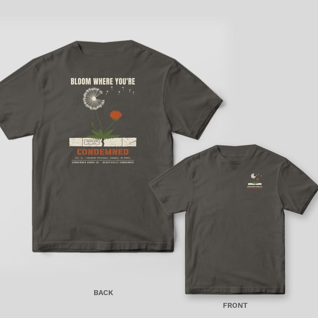 Pepper tee shown back and front: back has a dandelion with a cream seed head and rust flower growing through a sidewalk crack, reading Bloom Where You're Condemned.