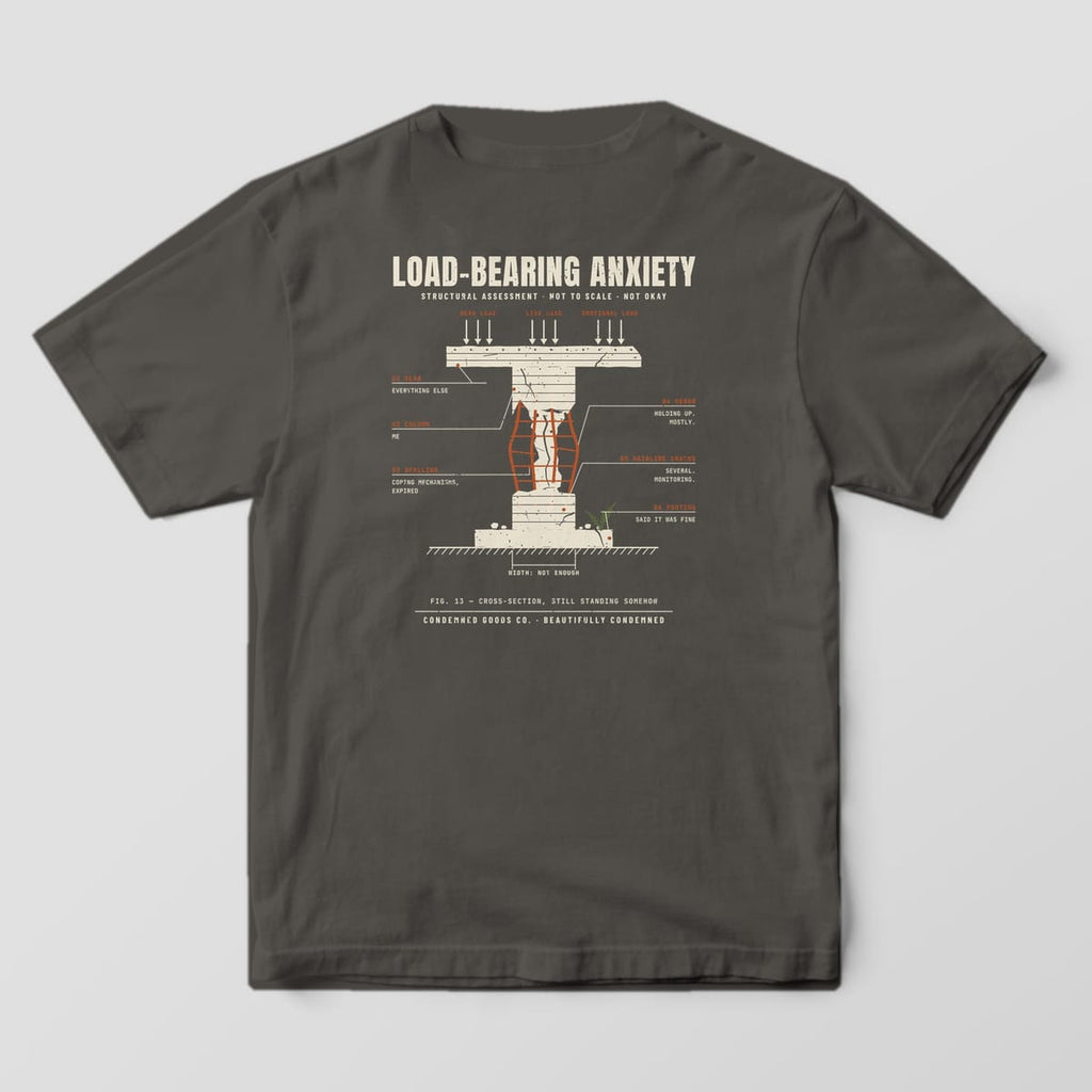 Back of a pepper Comfort Colors 1717 tee with a cream concrete column with exposed rust rebar and engineering callouts under the words Load-Bearing Anxiety.