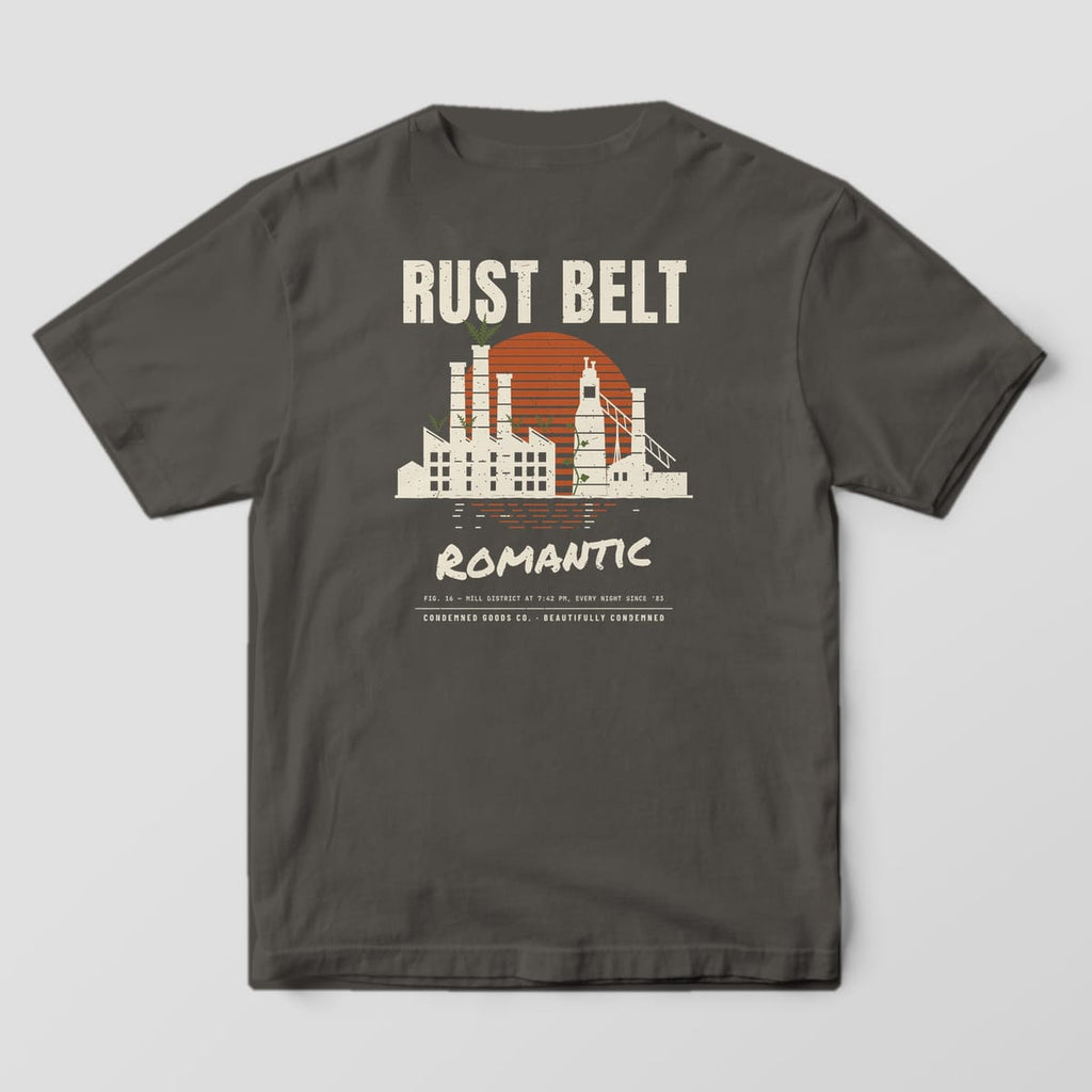 Back of a pepper Comfort Colors 1717 tee with a cream factory skyline with smokestacks against a striped rust sunset under the words Rust Belt Romantic.