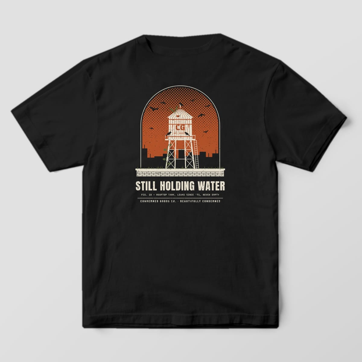 Back of a black Comfort Colors 1717 tee with a cream rooftop water tower against a rust dusk sky with crows under the words Still Holding Water.