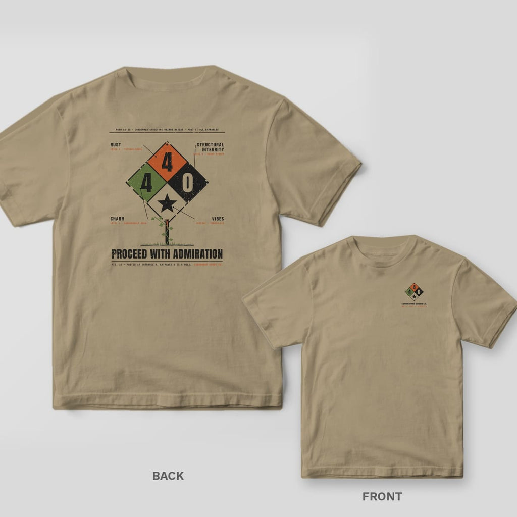 Khaki tee shown back and front: back has a weathered hazard diamond rating Rust 4, Charm 4, Structural Integrity 0 above the words Proceed With Admiration; front has a small four-color hazard diamond.