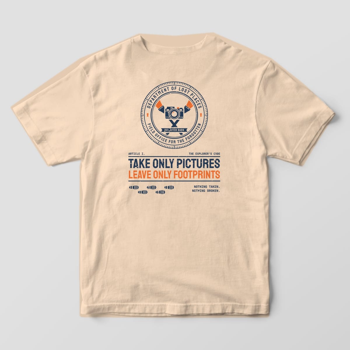 Back of an Ivory Comfort Colors 1717 tee printed with a navy and orange circular Dept. of Lost Places seal with a camera and crossed flashlights above the words Take Only Pictures, Leave Only Footprints and a trail of boot prints.