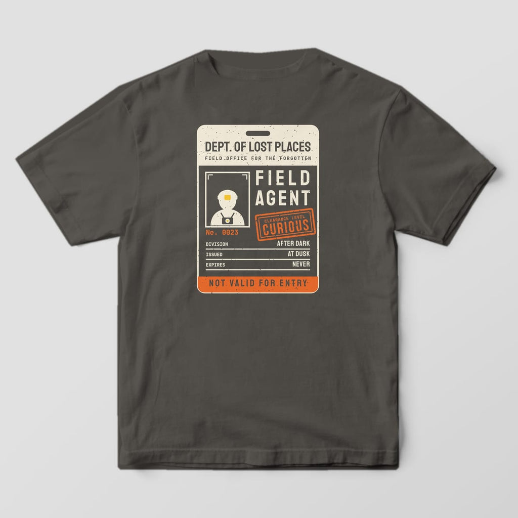 Back of a Pepper Comfort Colors 1717 tee printed with a cream, yellow and orange oversized ID card reading Dept. of Lost Places Field Agent with a headlamp explorer portrait and an orange Clearance Level Curious stamp.