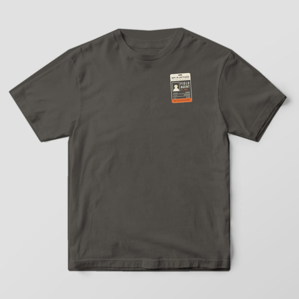 Front of a Pepper Comfort Colors 1717 tee with a small cream and orange Field Agent ID badge on the left chest.