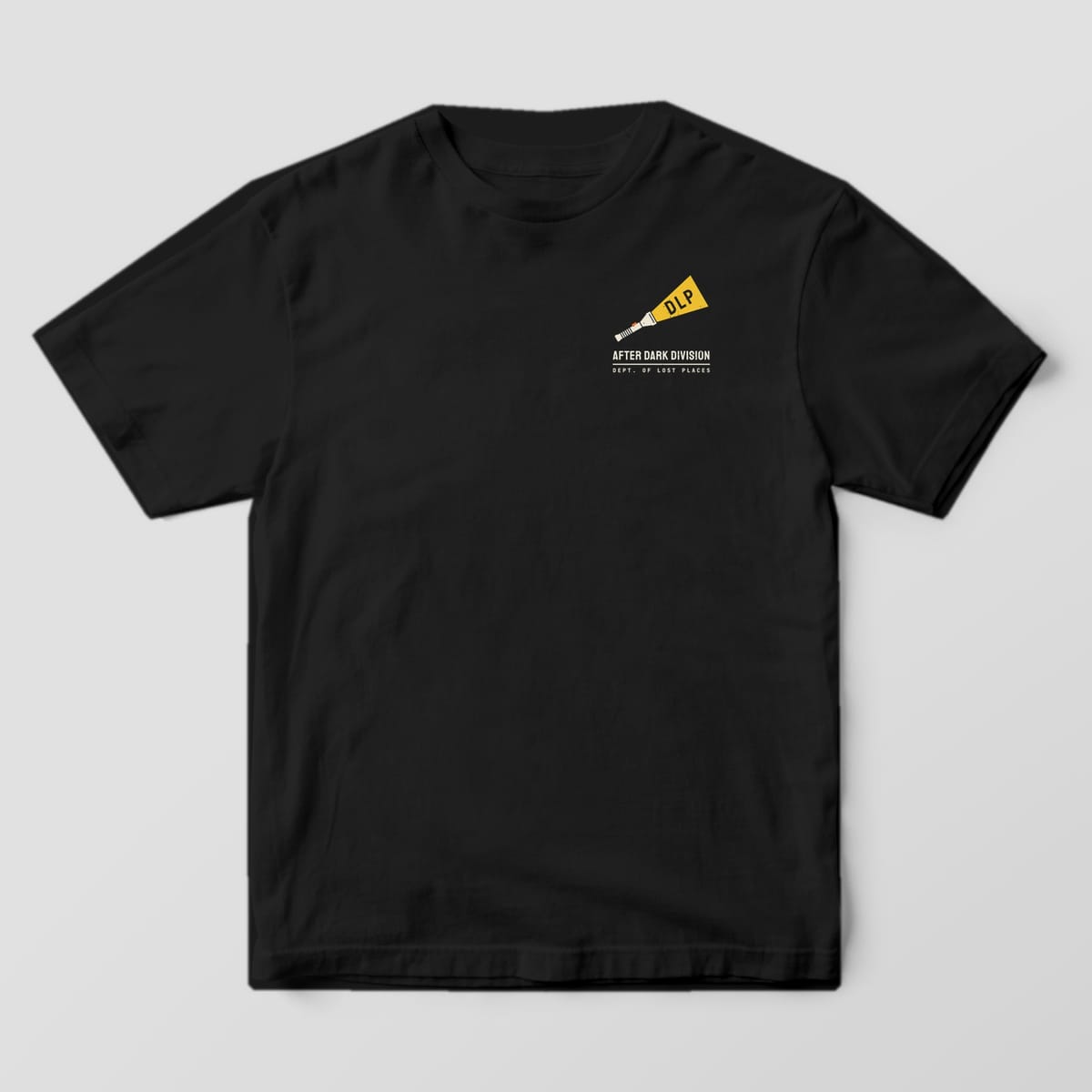 Front of a Black Comfort Colors 1717 tee with a small cream flashlight with a yellow beam containing the letters DLP above the words After Dark Division on the left chest.