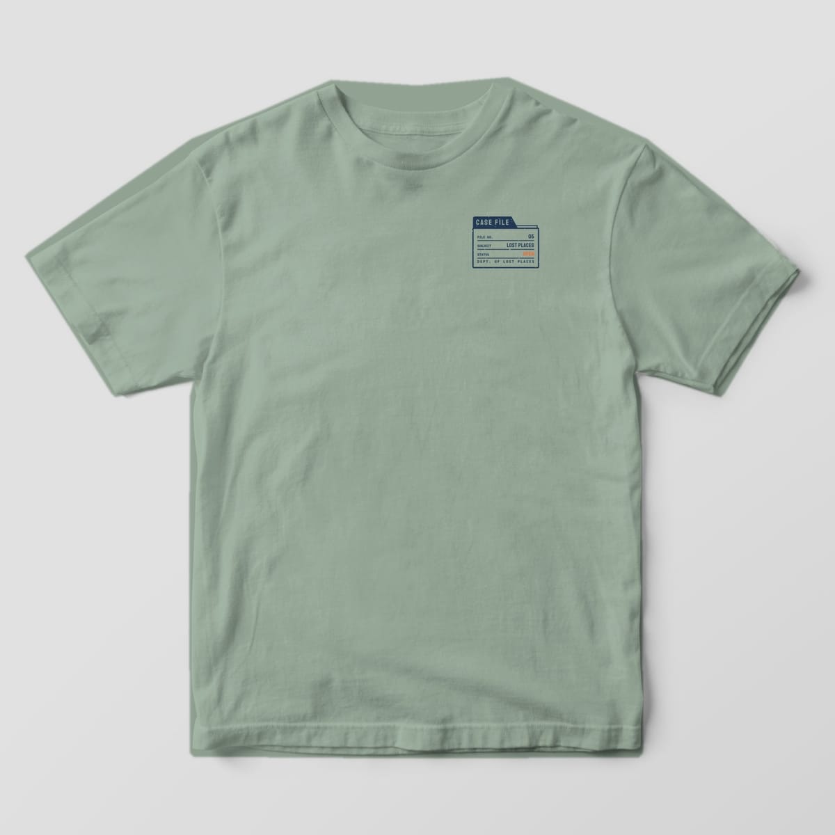 Front of a Bay Comfort Colors 1717 tee with a small navy file-folder tab reading Case File, Subject Lost Places, Status Open on the left chest.
