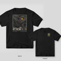 Black Comfort Colors tee shown back and front: the back has a cream topographic map with an orange dotted trail to a ruined house marked Here above Off the Map; the chest has a contour-line DLP badge.
