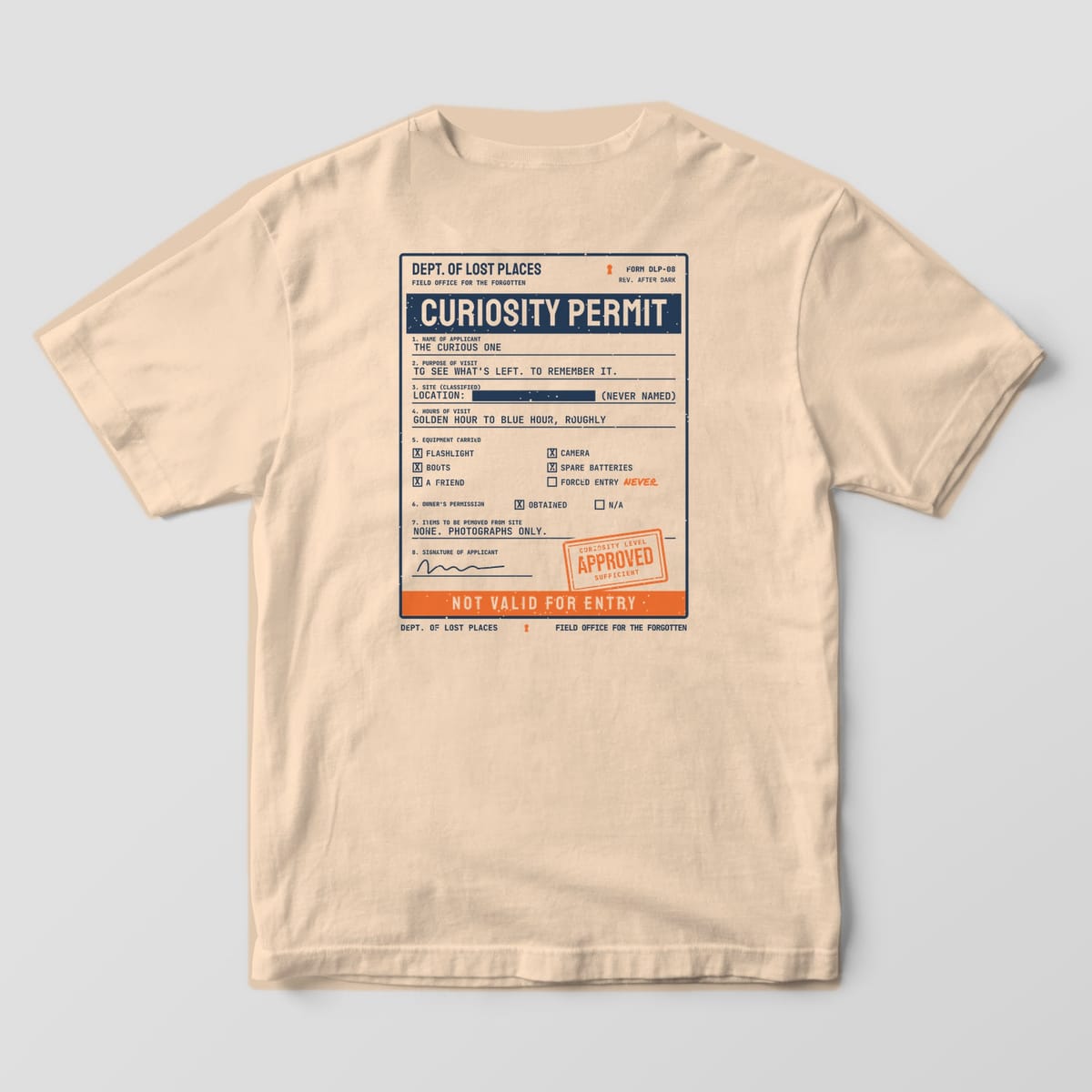 Back of an Ivory Comfort Colors 1717 tee printed with a navy typewritten Curiosity Permit form from the Dept. of Lost Places with checkboxes, a redacted site line, an orange Approved stamp and an orange Not Valid for Entry strip.