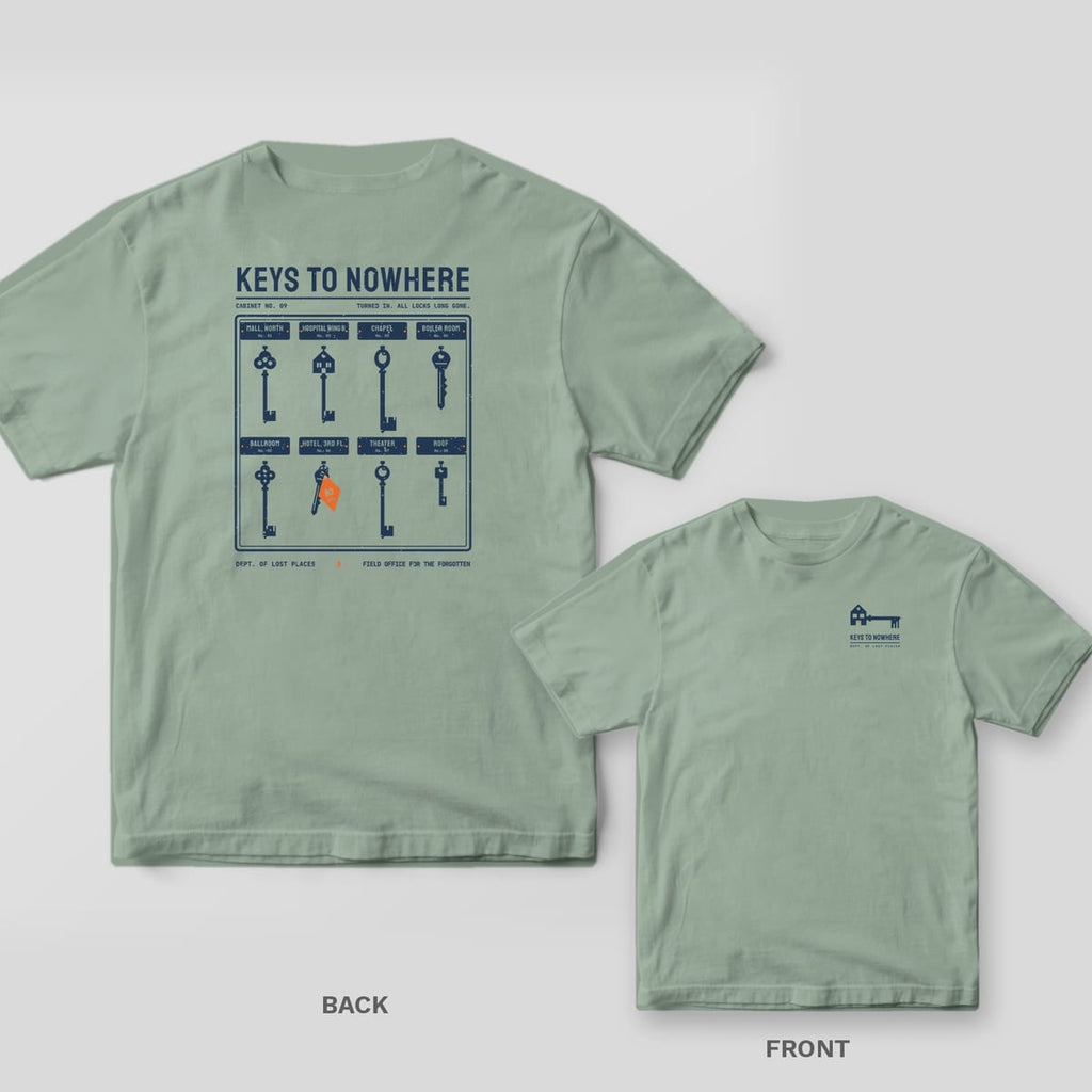Bay Comfort Colors tee shown back and front: the back has a navy key cabinet of eight vintage keys over name plates under Keys to Nowhere; the chest has a skeleton key with a house-shaped bow.