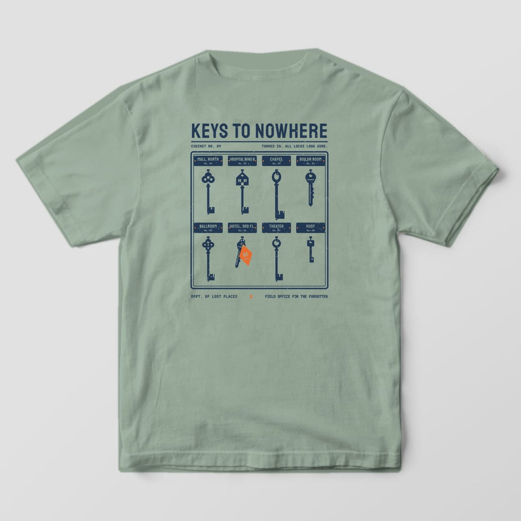 Back of a Bay Comfort Colors 1717 tee printed with a navy key cabinet holding eight vintage skeleton and hotel keys above name plates for places like Chapel, Ballroom and Roof, under the title Keys to Nowhere.