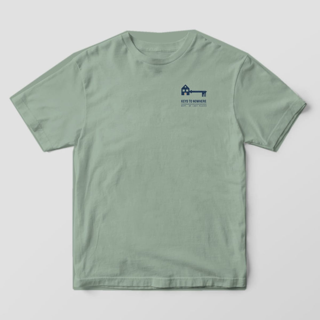 Front of a Bay Comfort Colors 1717 tee with a small navy skeleton key whose bow is shaped like a house above the words Keys to Nowhere on the left chest.