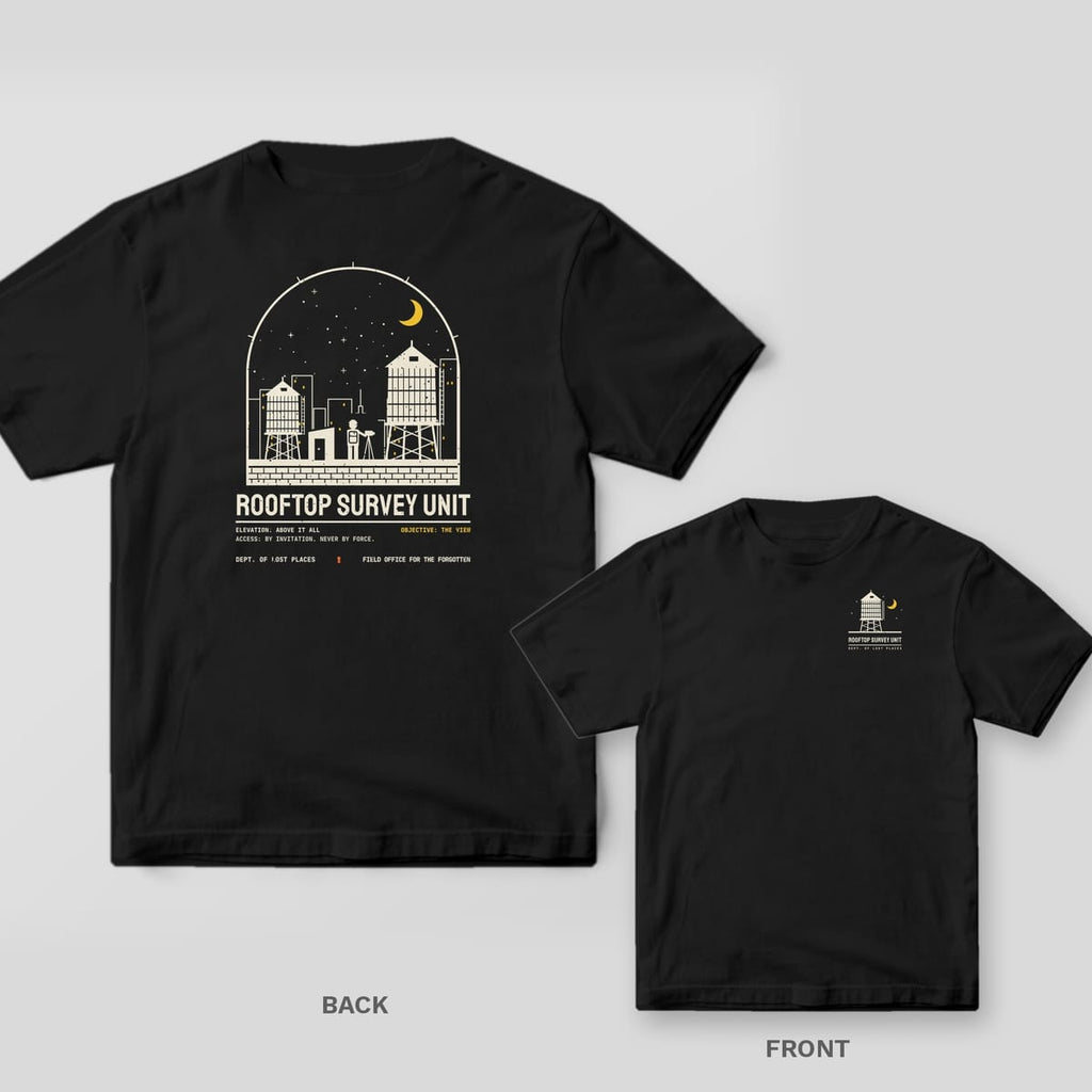 Black Comfort Colors tee shown back and front: the back has a cream and yellow night rooftop with water towers and a photographer at a tripod above Rooftop Survey Unit; the chest has a small water tower and moon.