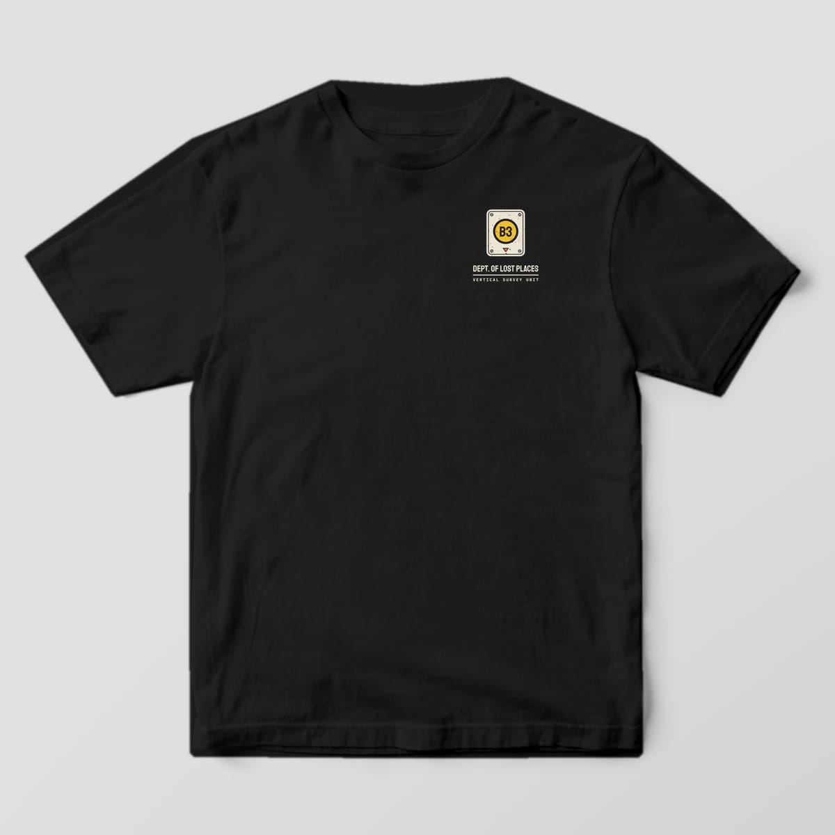 Front of a Black Comfort Colors 1717 tee with a small cream elevator button plate with a lit yellow B3 button above Dept. of Lost Places on the left chest.