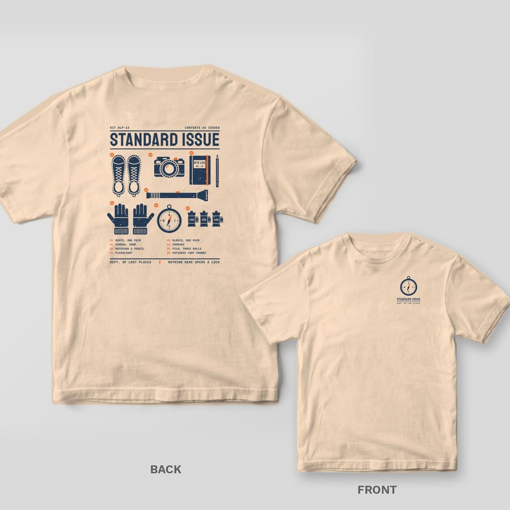 Ivory Comfort Colors tee shown back and front: the back has a navy and orange flat-lay of explorer gear under Standard Issue; the chest has a small compass.